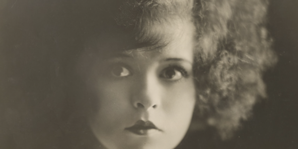 A black and white image of the silent star Clara Bow, with curly hair, looking at camera