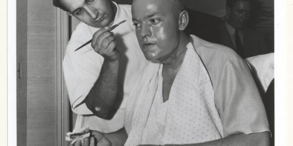 Orson Welles in makeup chair as artist applies old-age latex to his face