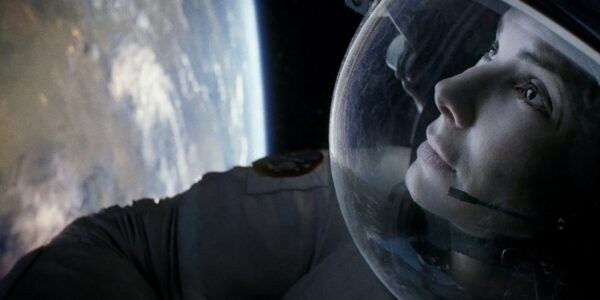 An astronaut's head inside her helmet as she floats in space, with the earth distant to the left