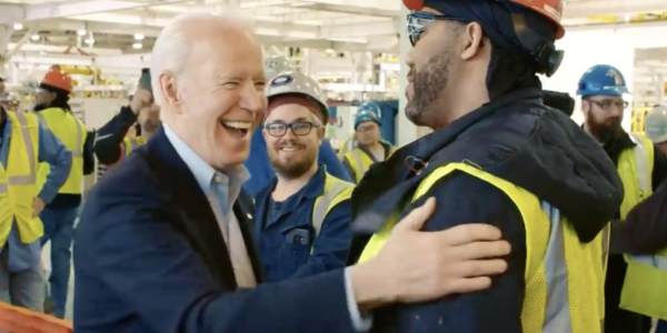 President Joe Biden on the left, putting his hand on the shoulder of a worker in a yellow vest and smiling