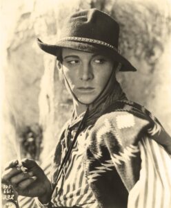 Rudolph Valentino in a hat and holding a cigarette, looking to the left of the camera