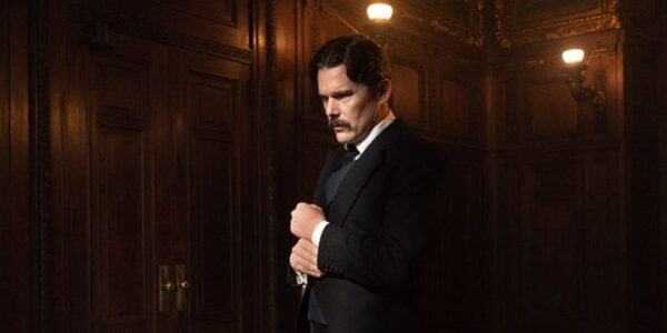 Ethan Hawke standing in a dark, oak room, holding his hands together