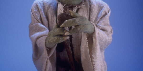 A full portrait of a puppet of Yoda from Star Wars, holding a cane