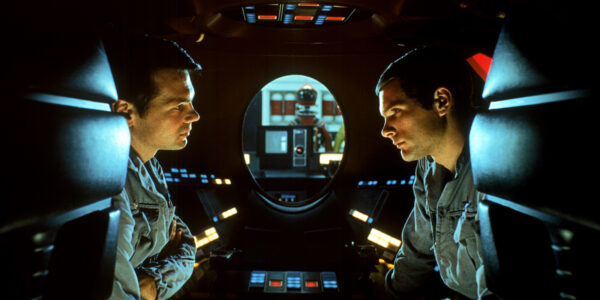 Two men speaking from the inside of space pod, their faces in profile