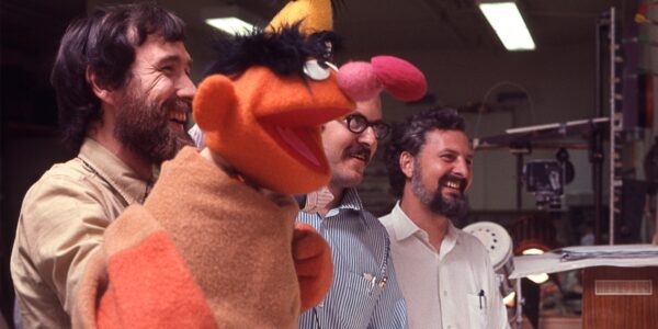 The puppet Ernie from Sesame Street being controlled in a behind the scenes image with puppeteers