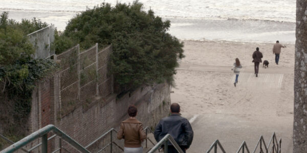 A couple walk down steps to a windswept beach