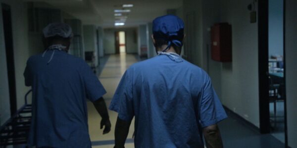 Doctors in the ER in scrubs, shown from behind walking down a hall