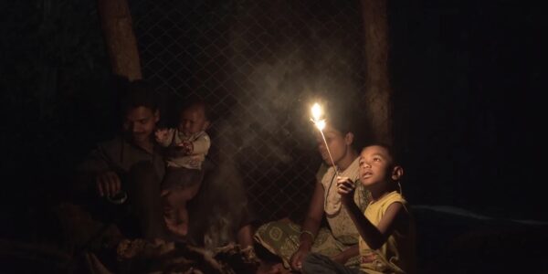 A child holding a sparkler in the dark, surrounded by family