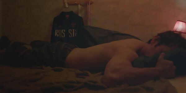A shirtless man lies face down on a bed in a dark room