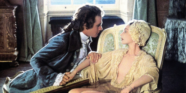 A man in a suit kneels next to a woman as she reclines in a bath, while draped in a robe, both in 18th century clothes