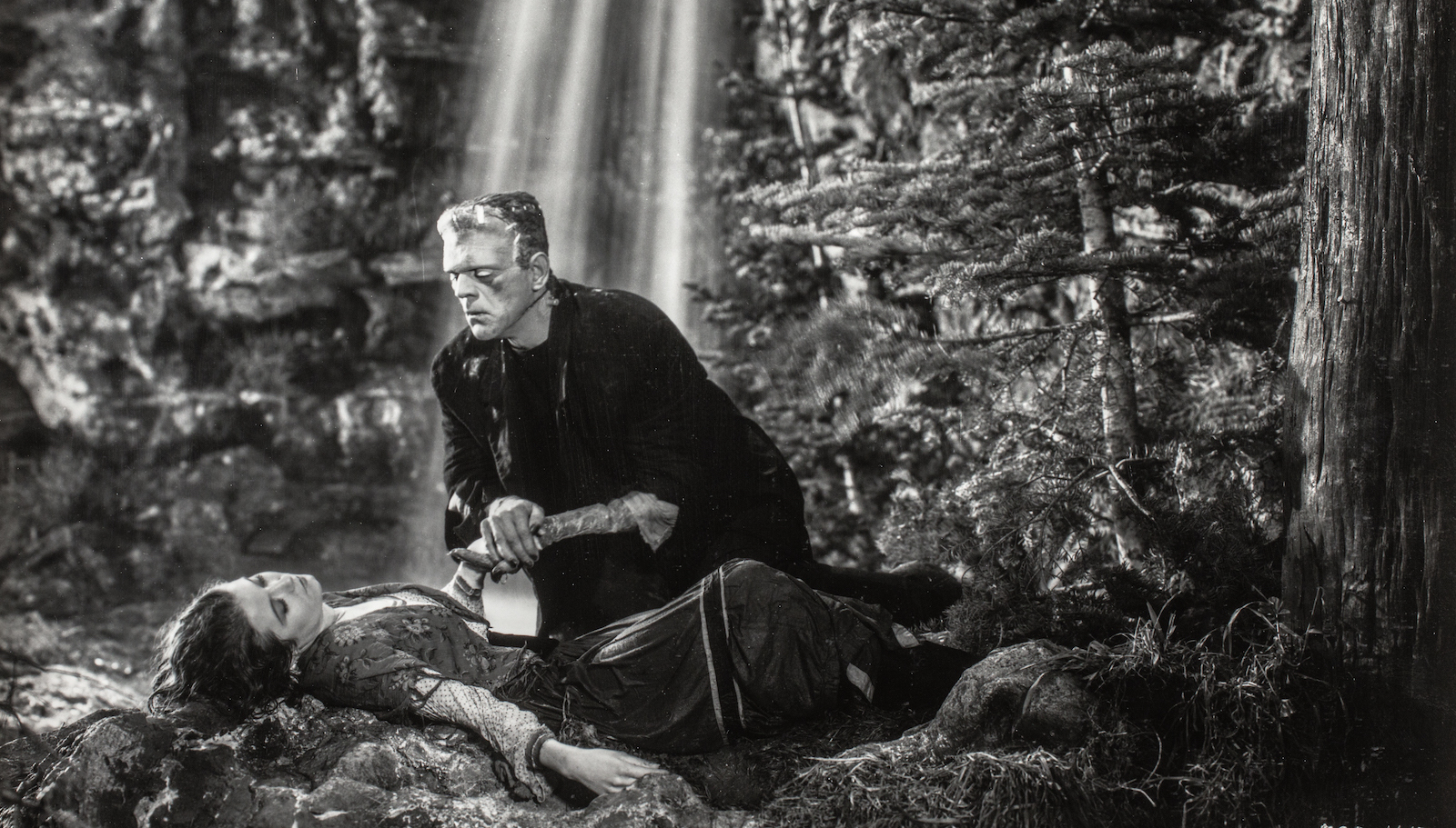 Frankenstein's monster stands over a reclining woman's body by a waterfall