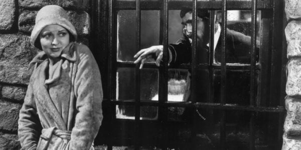 A man creepily reaches through a window's iron grate to grasp at a woman