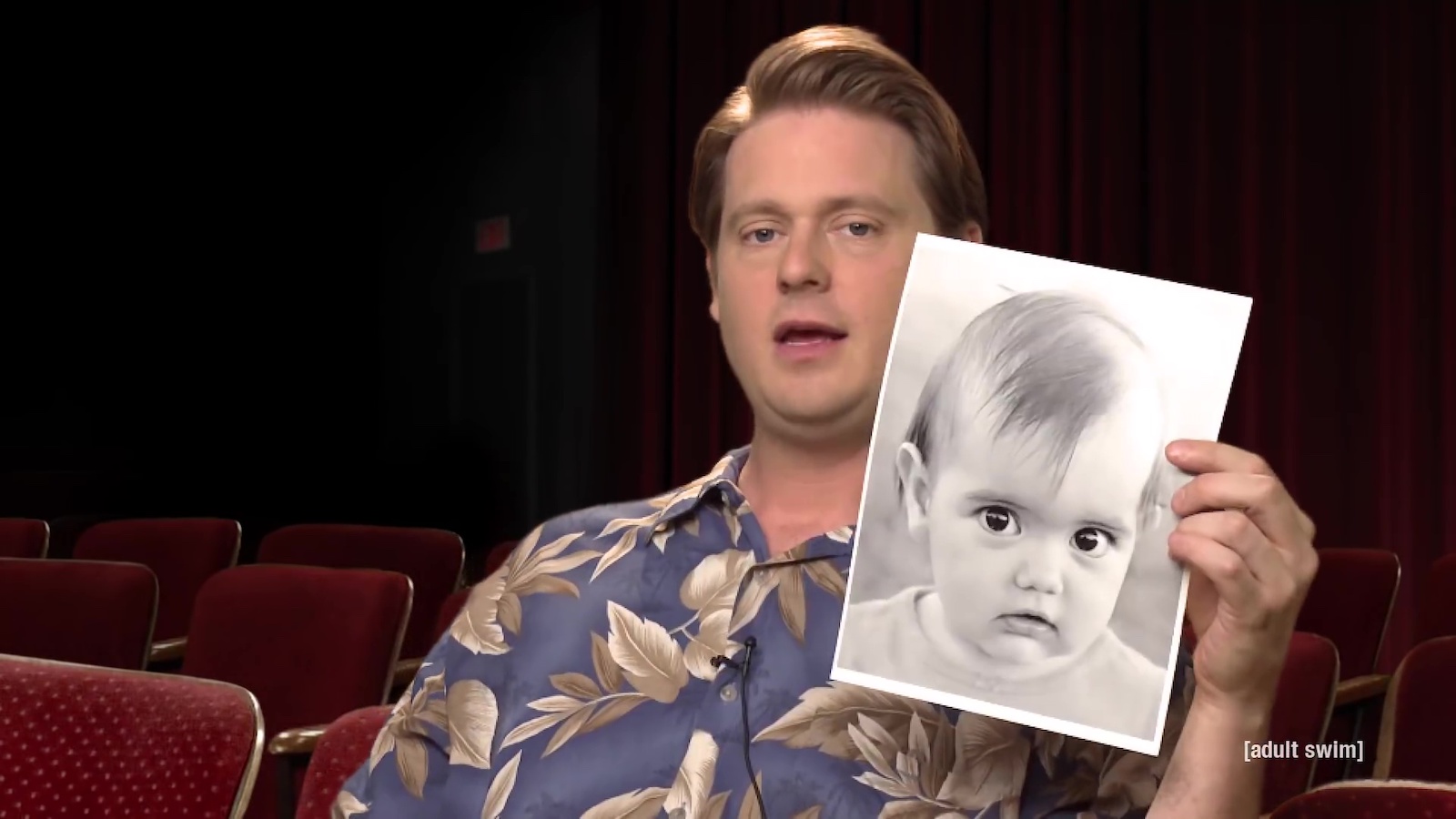 A man holds up a picture of a baby while talking to camera
