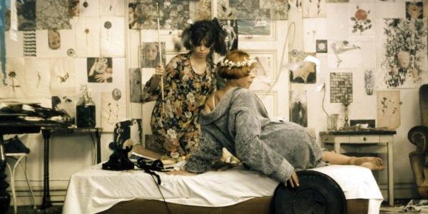 Two women on a bed with collage cutouts on the walls behind them