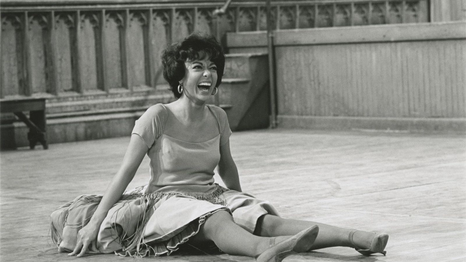 A smiling woman sits on the floor, taking a break from dancing.