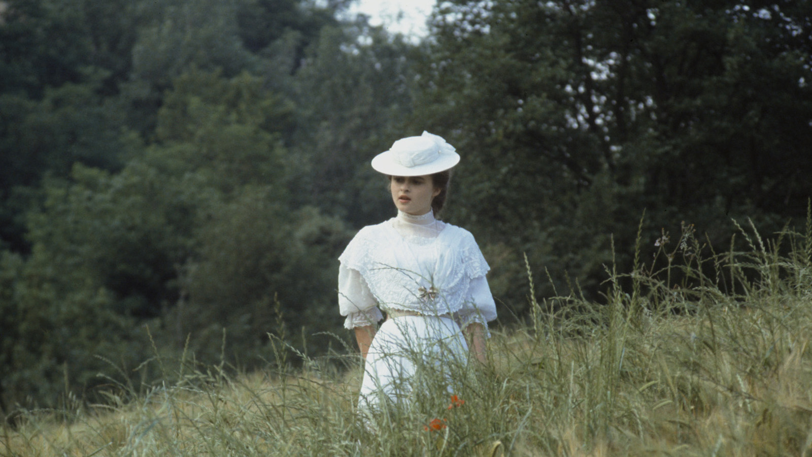 A woman in white stands in a lush green field.