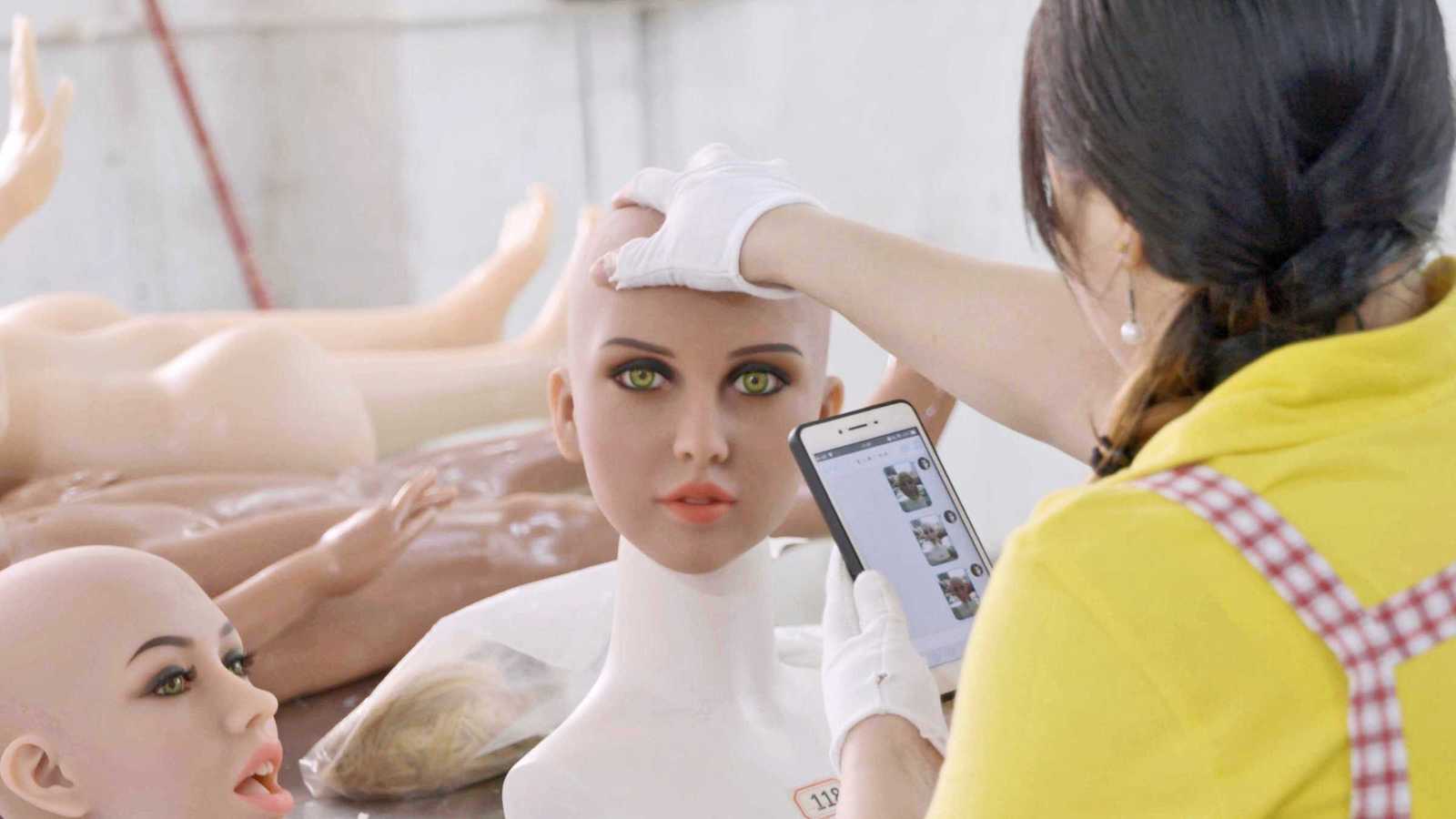 A factory worker holds the head of a plastic mannequin, which is directly facing the camera.