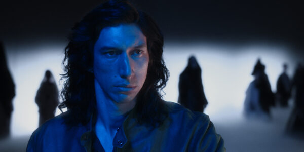 A man in long hair (Adam Driver) drenched in blue, looks past the camera in medium close-up, a dark silhouette in the background behind him.