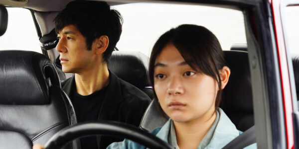 A woman with a serious expression drives a man, who sits in the back seat of the car.