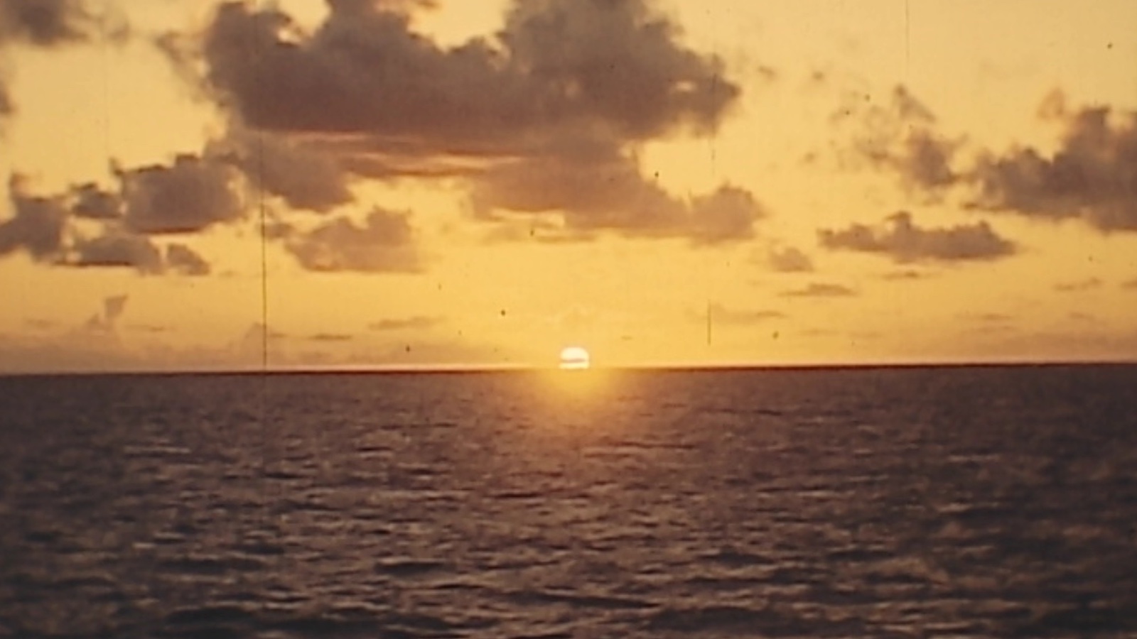 A sun sets on the yellow horizon across an expanse of sea.
