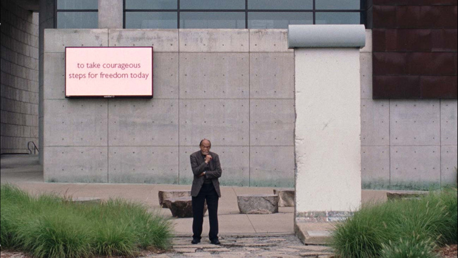 A man stands A man stands in front of a concrete building in front of a sign that says "to take courageous steps for freedom today"