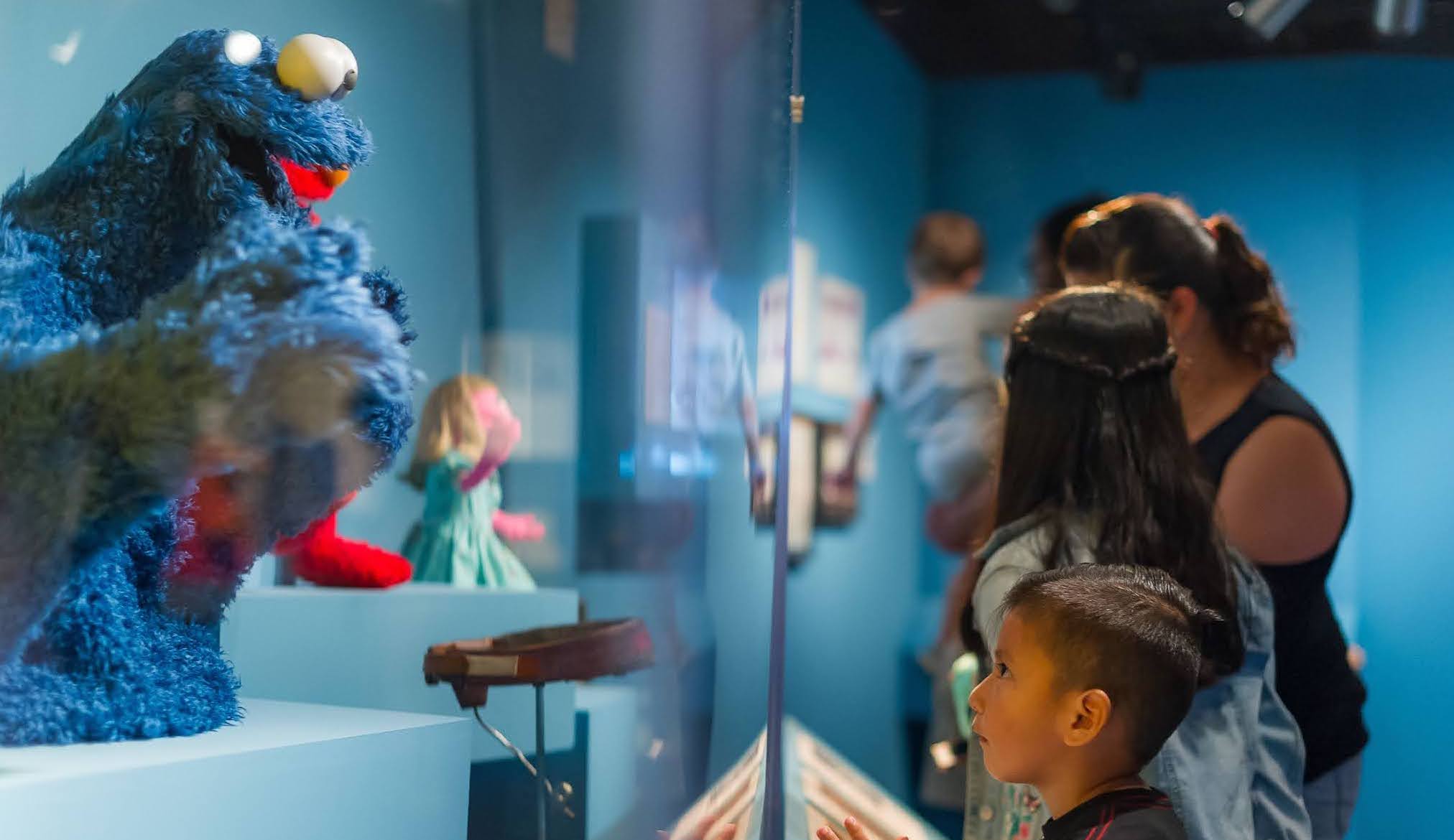 A little boy stares up at Cookie Monster in a class case at the Museum.