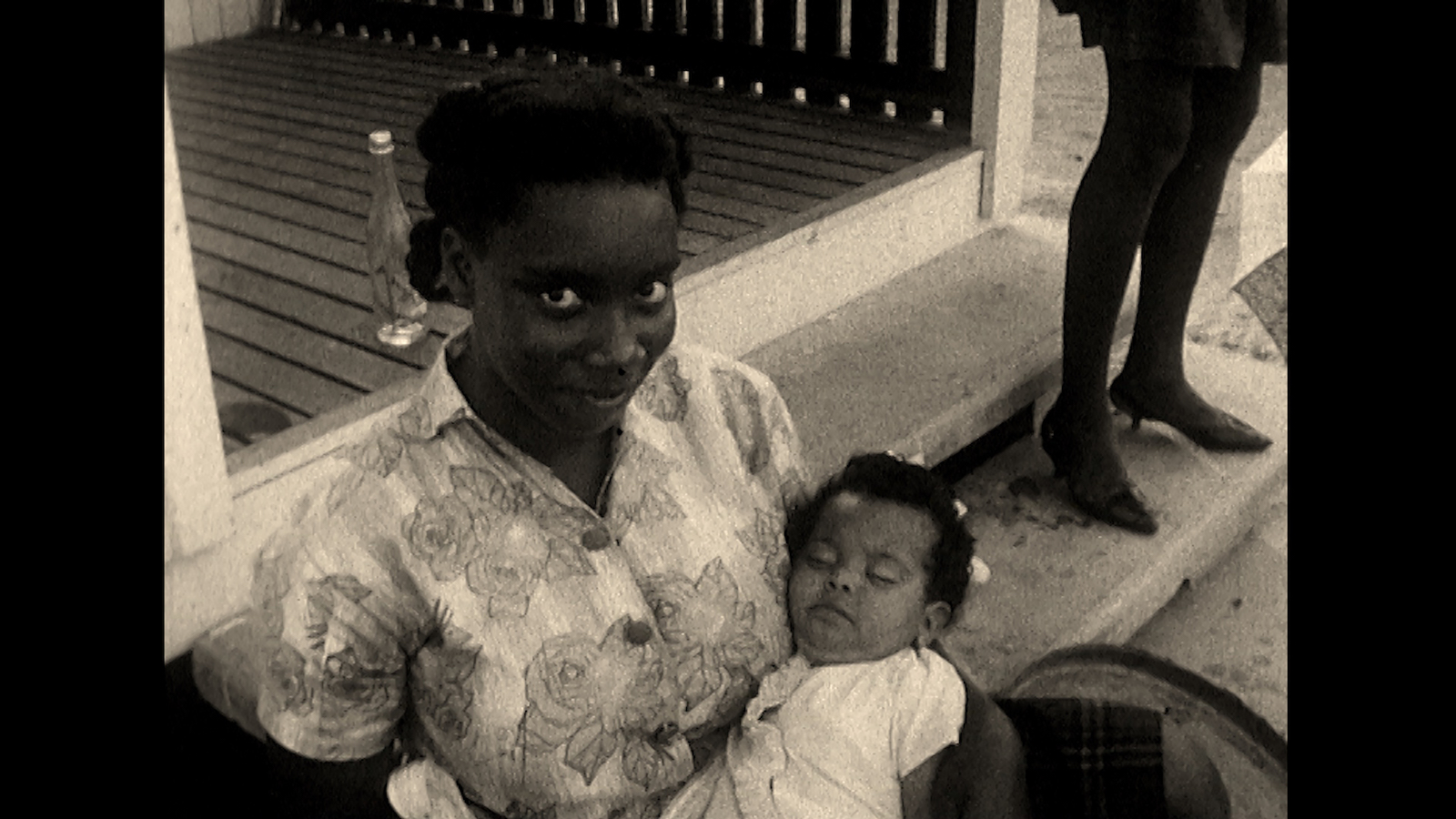 A smiling woman holds a baby and looks into the camera, in a black-and-white image