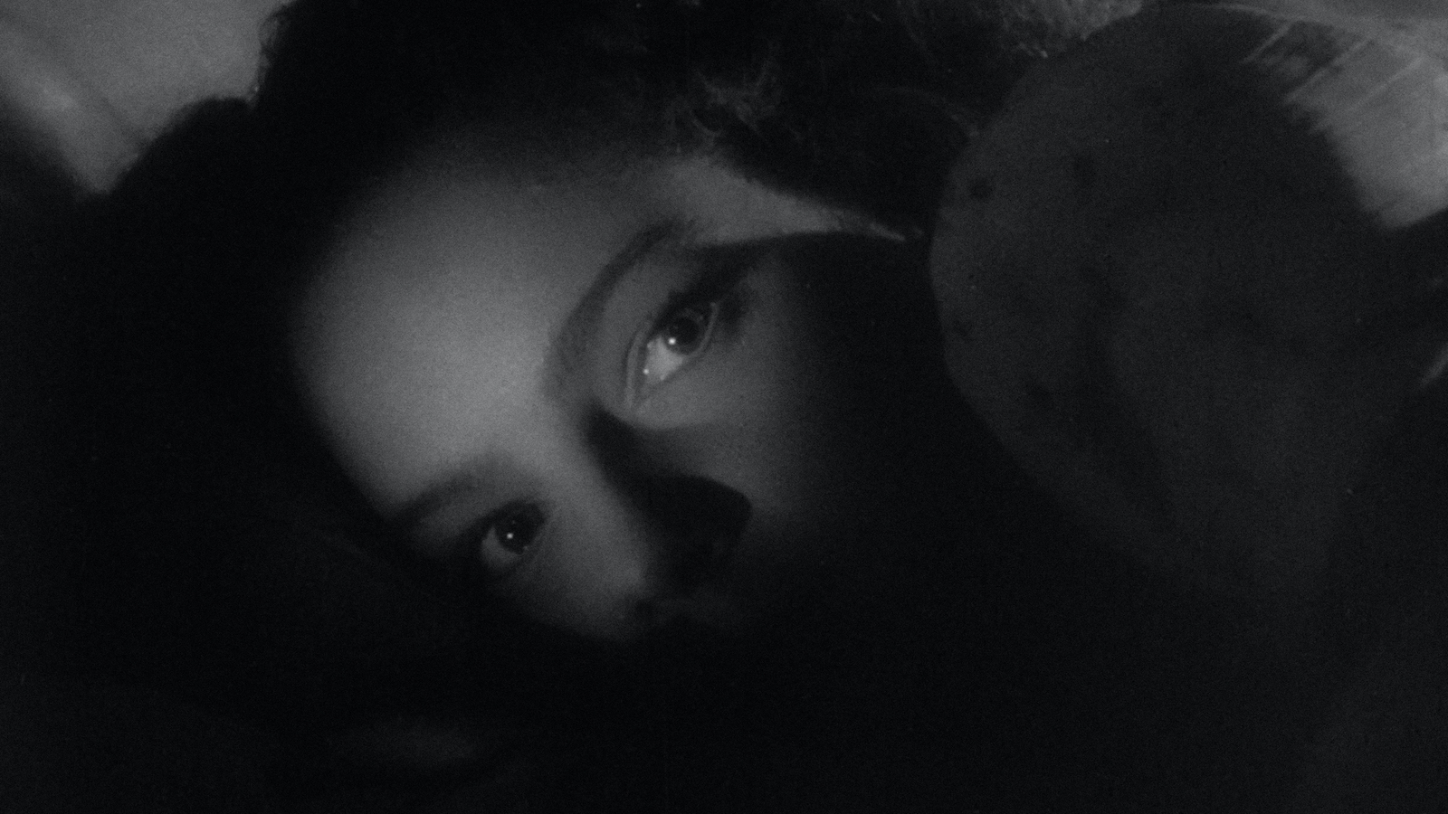 A woman's shadowed face in black-and-white looks off screen, her eyes illuminated