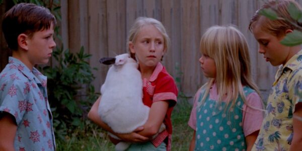A little blonde girl clutches a white rabbit while three other kids surround her.