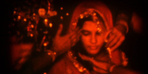 An image of a woman in a sari and veil, with hands surrounding her veil as she looks down