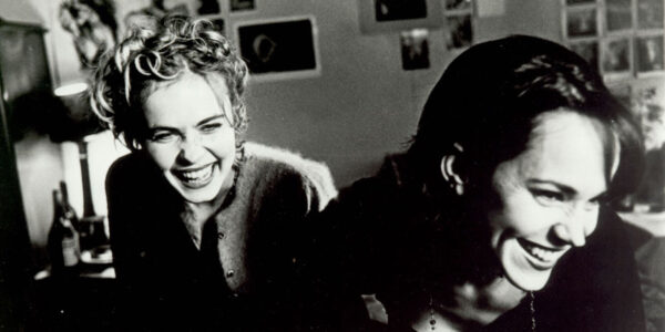 A black and white image of two women laughing, both facing camera, one slightly in back of the other.