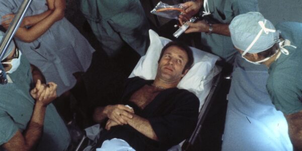 An overhead shot of a man , awake, on a surgery table surrounded by doctors