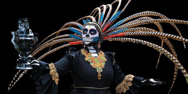 A person in a colorful costume and skeleton mask with feathers