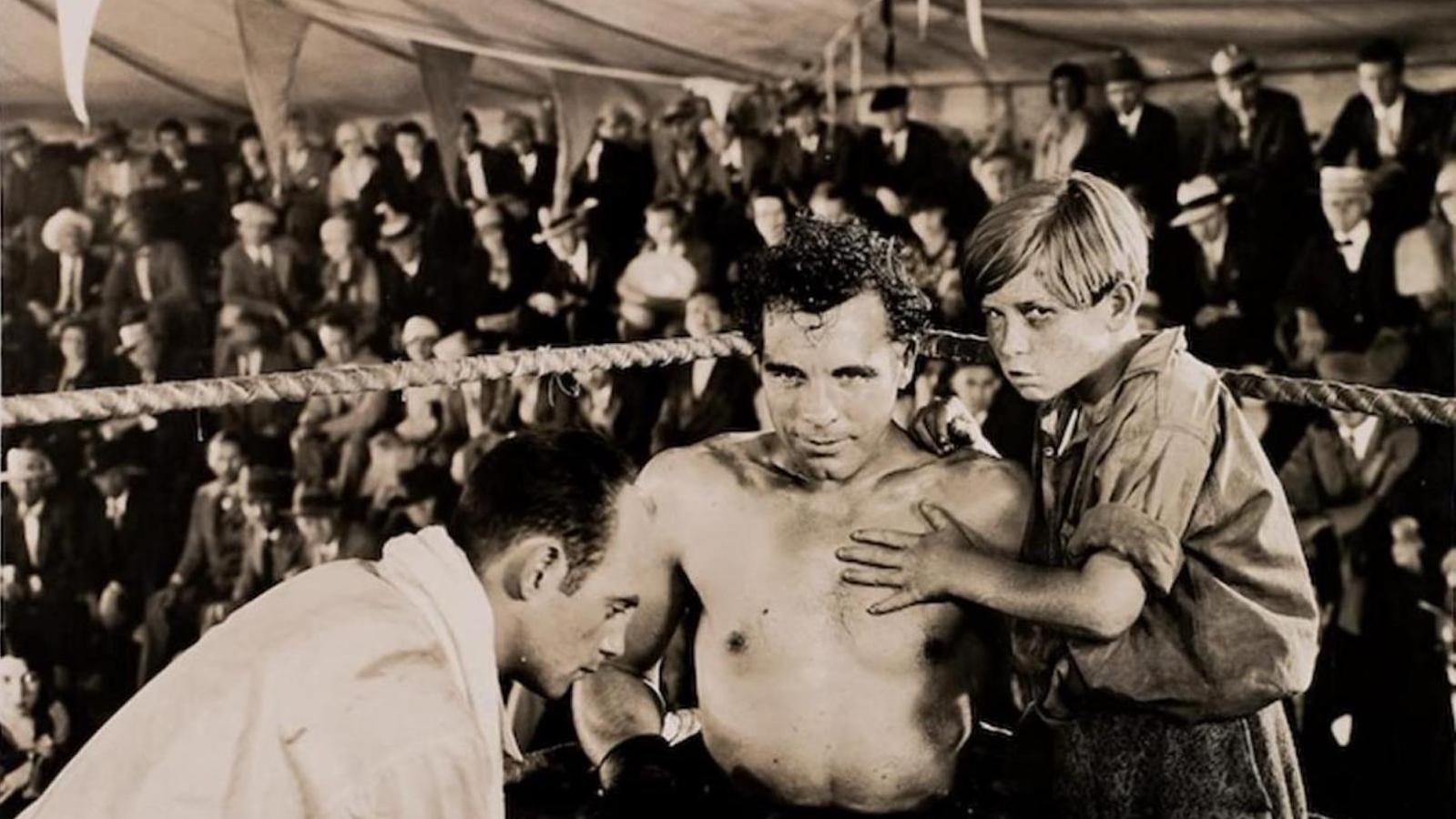 A boxer in the ring, looking at camera, beside a kid and his trainer.