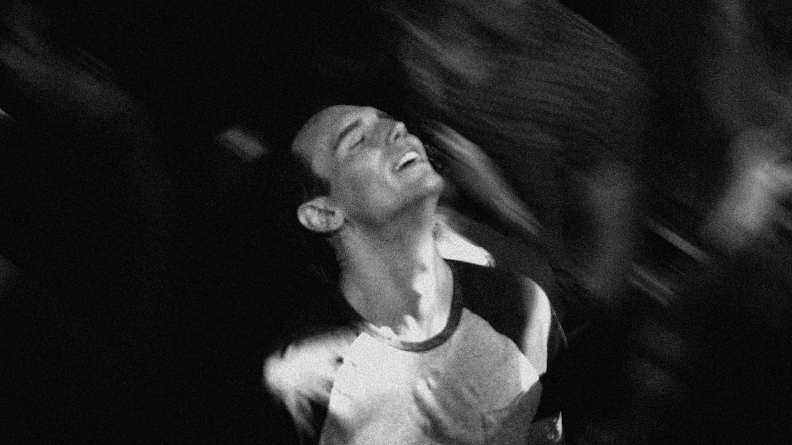 A black and white image of a young man looking up and ecstatically dancing