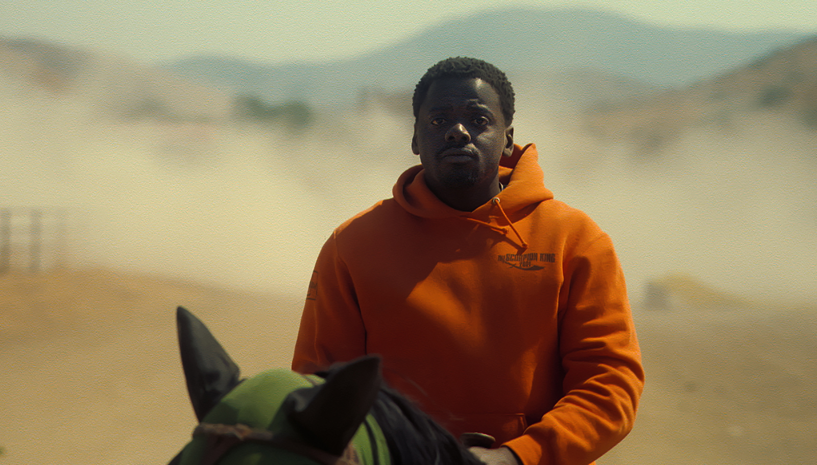 A man in an orange hoodie sweatshirt on a horse in a desert