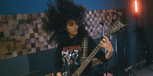 A woman plays guitar, her mass of black hair blown upwards