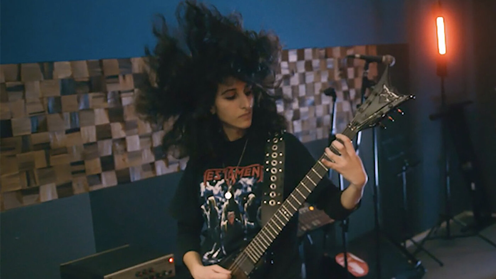 A woman plays guitar, her mass of black hair blown upwards