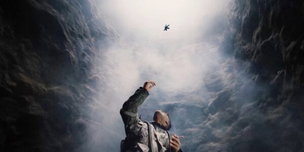 A man reaches up in the middle of a cave at floating leaves above his head