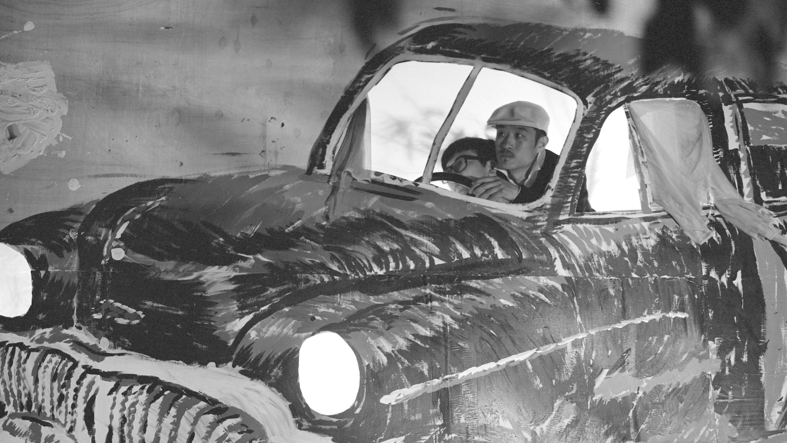 two men sit in the driver's seat of a cardboard illustrated car