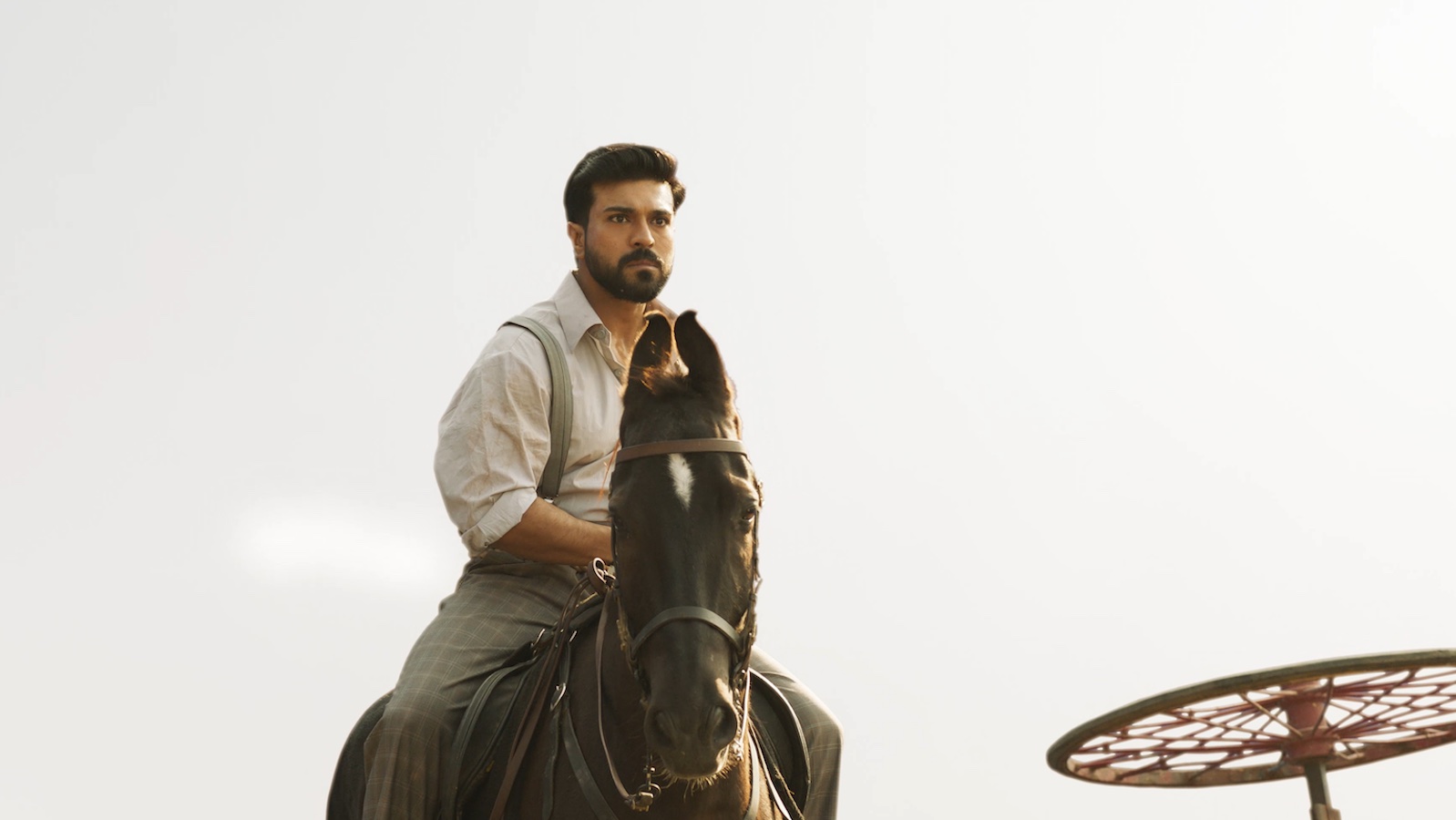 A bearded man in suspenders and a white shirt rides on horseback towards camera