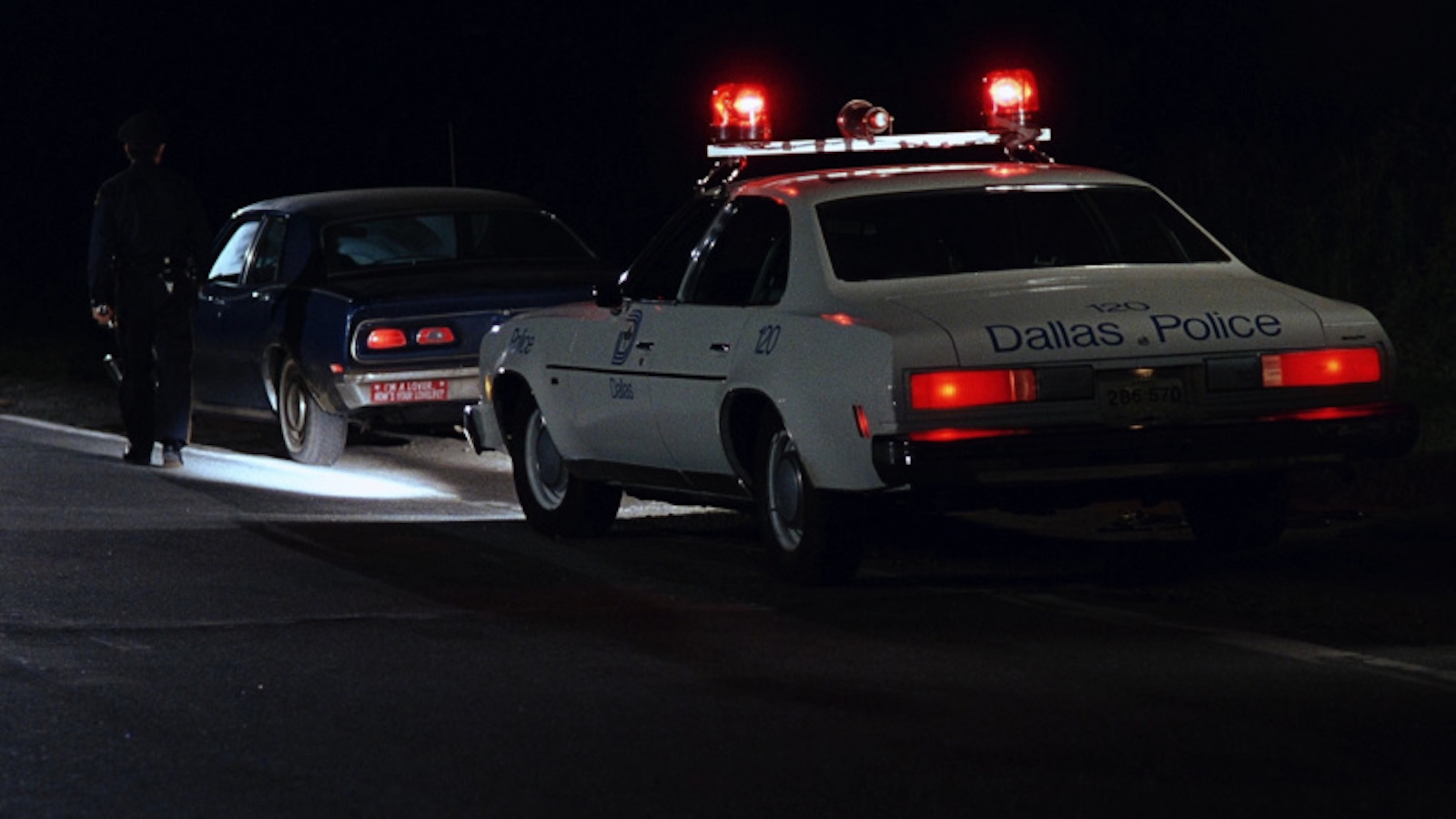 A police car with siren lights on pulls over a car at night