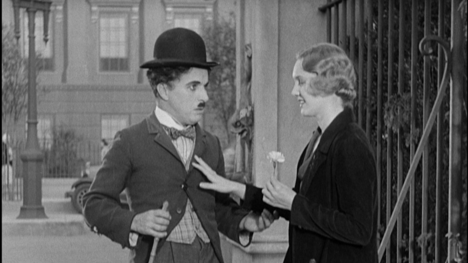 A little tramp in his bowler hat looks at a young woman holding a flower and smiling