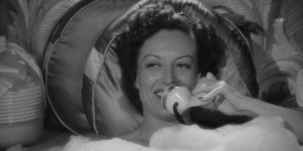 A smiling woman talks on the phone while taking a bubble bath