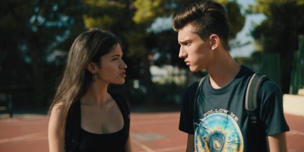 a young man and woman scowl and face each other on an outdoor basketball court