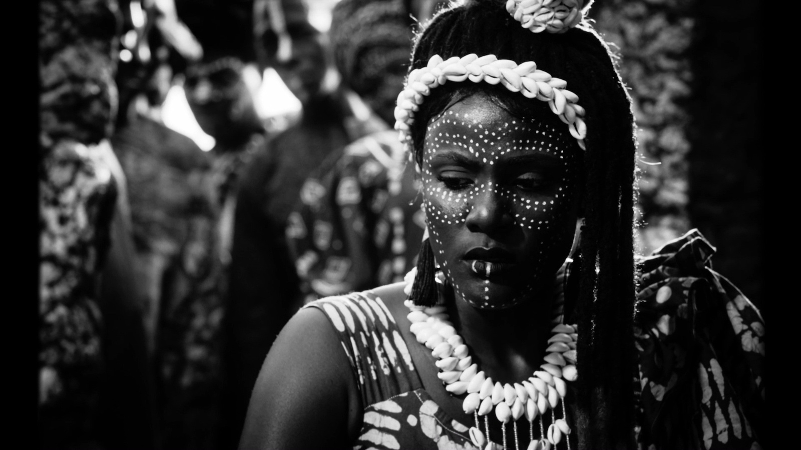 A woman in tribal makeup and headdress faces camera looking down