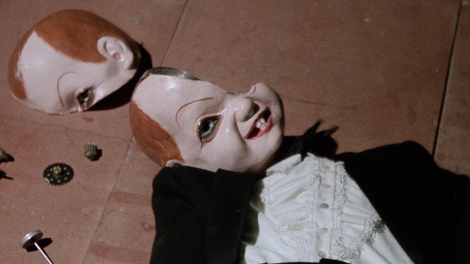 A broken dummy with its head cracked in two on the floor, looking up with a sinister expression