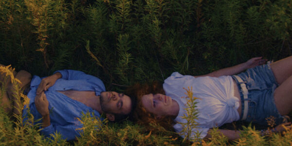 Two people lie a field with their heads touching but lying in opposite directions looking up