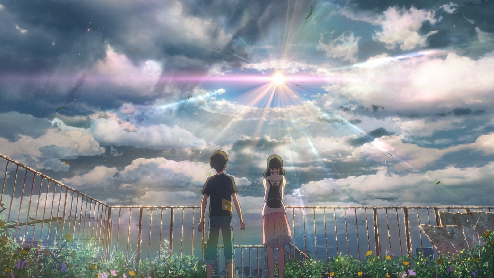 Two teenagers stand in a field and look up at a bright light breaking through clouds.