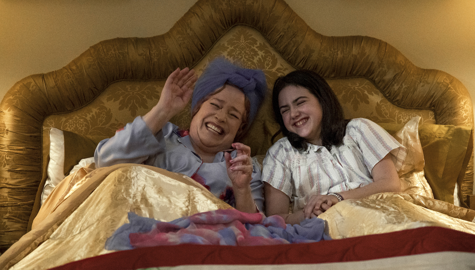 A mother and daughter laugh in bed together